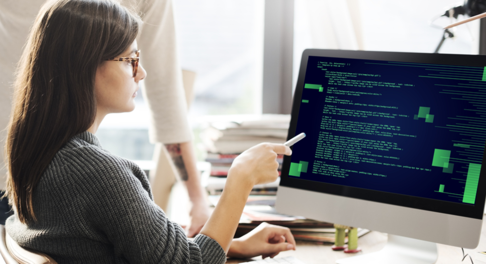 mujer señalando un código en la pantalla de una computadora