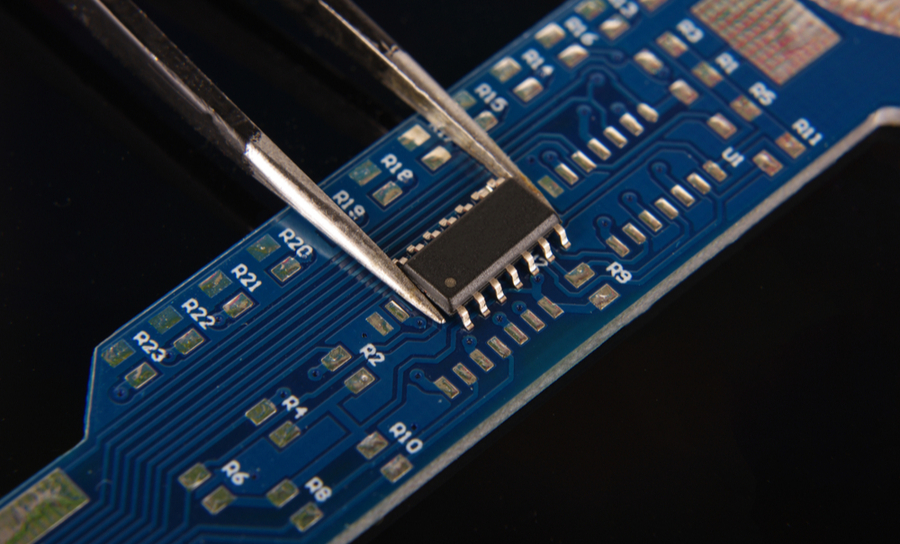 Black IC in tweezers on a blue PCB