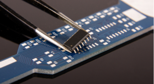 Surface mount IC in tweezers over a blue PCB